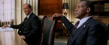 Movie still from “Shooter” (2007), directed by Antoine Fuqua – A man in a suit and tie sitting in a chair; Close Up shot, Over the shoulder angle
