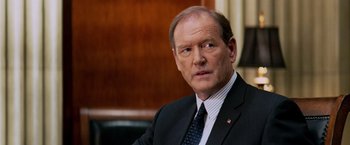 Movie still from “Shooter” (2007), directed by Antoine Fuqua – A man in a suit and tie sitting in front of a wooden wall; Close Up shot, Over the shoulder angle
