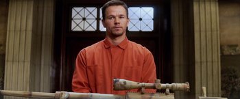 Movie still from “Shooter” (2007), directed by Antoine Fuqua – A man in an orange shirt is standing in front of a rifle; Medium shot, Low angle