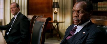 Movie still from “Shooter” (2007), directed by Antoine Fuqua – A man in a suit and tie sitting in front of a chair; Close Up shot, Over the shoulder angle