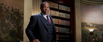 Movie still from “Shooter” (2007), directed by Antoine Fuqua – A man in a suit and tie in front of a book shelf; Medium shot, Low angle