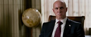 Movie still from “Shooter” (2007), directed by Antoine Fuqua – A man in a suit and tie sitting in front of a globe; Close Up shot, Over the shoulder angle