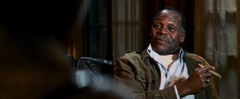 Movie still from “Shooter” (2007), directed by Antoine Fuqua – An older man sitting in a chair looking at the camera; Close Up shot, Over the shoulder angle