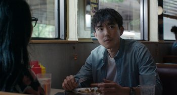 Movie still from “Shortcomings” (2023), directed by Randall Park – A man sitting in front of a plate of food; Close Up shot, Over the shoulder angle