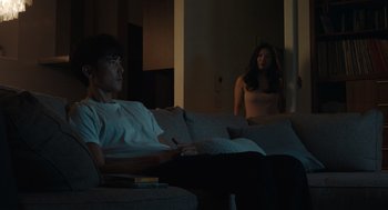 Movie still from “Shortcomings” (2023), directed by Randall Park – A man and a woman sitting on a couch in a living room; Medium shot, Over the shoulder angle