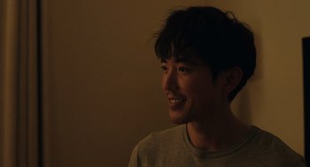 Movie still from “Shortcomings” (2023), directed by Randall Park – A young man smiles brightly while posing for a picture; Close Up shot, Over the shoulder angle