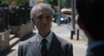 Movie still from “Shortcomings” (2023), directed by Randall Park – An older man wearing a suit and tie on the street; Close Up shot, Over the shoulder angle