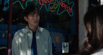 Movie still from “Shortcomings” (2023), directed by Randall Park – A man standing in front of a video store window; Medium shot, Over the shoulder angle