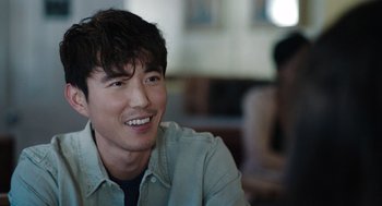 Movie still from “Shortcomings” (2023), directed by Randall Park – A young man smiles while sitting at a table; Close Up shot, Over the shoulder angle