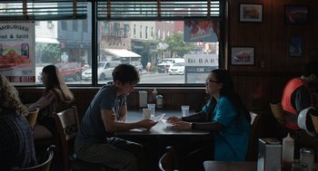 Movie still from “Shortcomings” (2023), directed by Randall Park – A man and a woman sitting at a table in front of a window; Medium shot, Over the shoulder angle