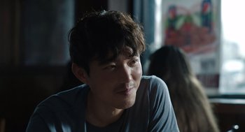 Movie still from “Shortcomings” (2023), directed by Randall Park – A young man with dark hair sitting at a table; Close Up shot, Over the shoulder angle