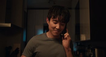 Movie still from “Shortcomings” (2023), directed by Randall Park – A man talking on a cell phone while standing in a kitchen; Close Up shot, Over the shoulder angle