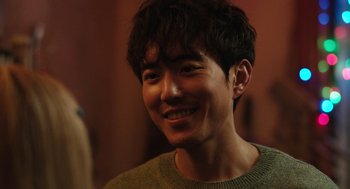 Movie still from “Shortcomings” (2023), directed by Randall Park – A young man smiles brightly while wearing a sweater; Close Up shot, Over the shoulder angle