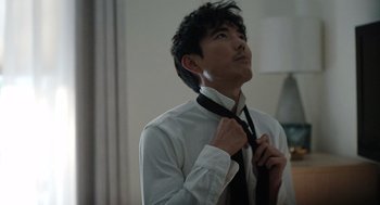 Movie still from “Shortcomings” (2023), directed by Randall Park – A man in white shirt and black tie adjusting his neck tie; Medium shot, Over the shoulder angle