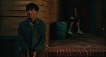 Movie still from “Shortcomings” (2023), directed by Randall Park – A man sitting on the steps of a brick building; Medium shot, Over the shoulder angle