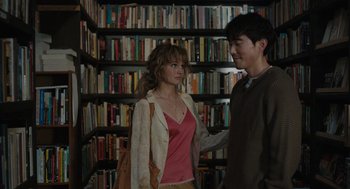 Movie still from “Shortcomings” (2023), directed by Randall Park – A man and a woman standing next to each other in front of a book shelf; Medium shot, Over the shoulder angle