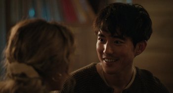 Movie still from “Shortcomings” (2023), directed by Randall Park – A man smiling at the camera while a woman looks on; Close Up shot, Over the shoulder angle