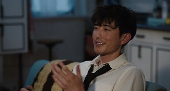 Movie still from “Shortcomings” (2023), directed by Randall Park – A young man wearing a white shirt and a black neck tie clapping his hands; Close Up shot, Over the shoulder angle