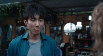 Movie still from “Shortcomings” (2023), directed by Randall Park – A young man in a blue shirt is standing in a room; Close Up shot, Over the shoulder angle