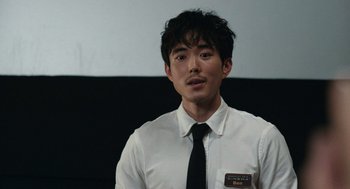 Movie still from “Shortcomings” (2023), directed by Randall Park – A man wearing a white shirt and a black tie; Medium shot, Over the shoulder angle