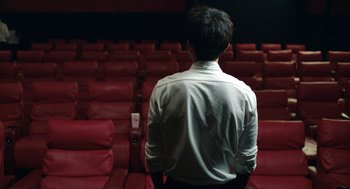 Movie still from “Shortcomings” (2023), directed by Randall Park – A man standing in front of a red theater seat; Medium shot, Over the shoulder angle