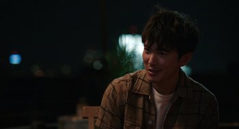 Movie still from “Shortcomings” (2023), directed by Randall Park – A man sitting on top of a wooden bench at night; Close Up shot, Over the shoulder angle