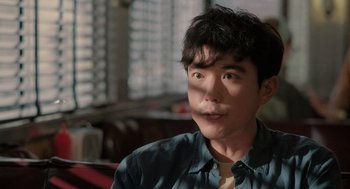 Movie still from “Shortcomings” (2023), directed by Randall Park – A young man with short black hair is looking at the camera; Close Up shot, Over the shoulder angle