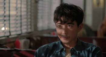 Movie still from “Shortcomings” (2023), directed by Randall Park – A man with a beard is smiling for the camera; Close Up shot, Over the shoulder angle