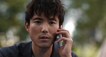 Movie still from “Shortcomings” (2023), directed by Randall Park – A young man is talking on a cell phone; Close Up shot, Over the shoulder angle
