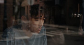 Movie still from “Shortcomings” (2023), directed by Randall Park – A young man looking out a window at the street; Close Up shot, High angle