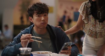 Movie still from “Shortcomings” (2023), directed by Randall Park – A man sitting at a table with chopsticks in his hands; Medium shot, Over the shoulder angle