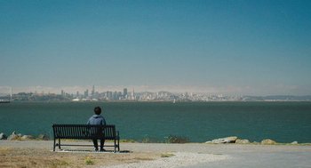 Movie still from “Shortcomings” (2023), directed by Randall Park – A person sitting on a bench looking out at the ocean; Extreme Wide shot, Over the shoulder angle