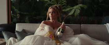 Movie still from “Shotgun Wedding” (2022), directed by Jason Moore – A woman sitting on a couch holding a bottle of champagne; Medium shot, Over the shoulder angle