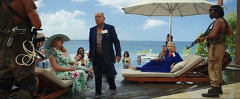 Movie still from “Shotgun Wedding” (2022), directed by Jason Moore – A man in a suit walking through the water at a beach party; Wide shot, Over the shoulder angle