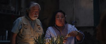 Movie still from “Shotgun Wedding” (2022), directed by Jason Moore – An older man standing next to an older woman in front of plants; Medium shot, Low angle
