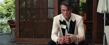 Movie still from “Shotgun Wedding” (2022), directed by Jason Moore – A man wearing a suit and tie sitting on the ground; Medium shot, Over the shoulder angle