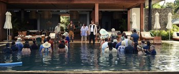 Movie still from “Shotgun Wedding” (2022), directed by Jason Moore – A group of people sitting in a pool watching a performer; Extreme Wide shot, High angle