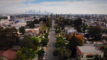 Movie still from “Show Me the Father” (2021), directed by Rick Altizer – An aerial view of a residential neighborhood with a city skyline in the background; Extreme Wide shot, High angle