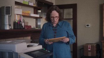 Movie still from “Showing Up” (2022), directed by Kelly Reichardt – A woman standing in front of an open envelope; Medium shot, Low angle