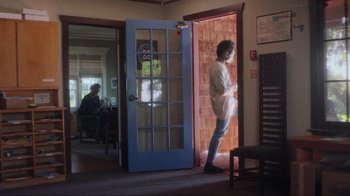 Movie still from “Showing Up” (2022), directed by Kelly Reichardt – A man standing in front of an open blue door; Wide shot, Over the shoulder angle