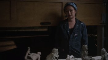 Movie still from “Showing Up” (2022), directed by Kelly Reichardt – A woman standing in front of a table; Medium shot, Over the shoulder angle