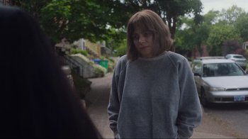 Movie still from “Showing Up” (2022), directed by Kelly Reichardt – A woman in a gray sweatshirt is standing on the sidewalk; Medium shot, Over the shoulder angle