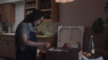 Movie still from “Showing Up” (2022), directed by Kelly Reichardt – A woman opening a box in a kitchen; Medium shot, Over the shoulder angle