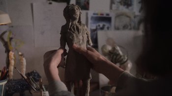 Movie still from “Showing Up” (2022), directed by Kelly Reichardt – A person is holding a clay statue in their hands; Extreme Close Up shot, Over the shoulder angle