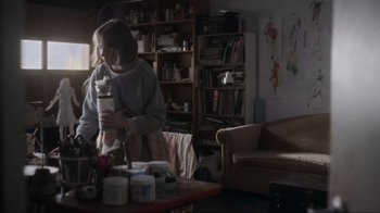 Movie still from “Showing Up” (2022), directed by Kelly Reichardt – A woman in a living room holding a coffee mug; Medium shot, High angle