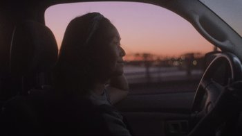 Movie still from “Showing Up” (2022), directed by Kelly Reichardt – A woman sitting in a car looking out the window at dusk; Close Up shot, Over the shoulder angle