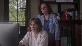 Movie still from “Showing Up” (2022), directed by Kelly Reichardt – A woman sitting next to another woman at a computer desk; Medium shot, Over the shoulder angle