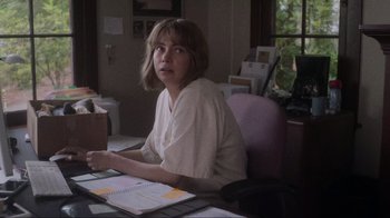Movie still from “Showing Up” (2022), directed by Kelly Reichardt – A woman sitting at a desk in front of a notebook; Medium shot, High angle