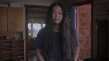 Movie still from “Showing Up” (2022), directed by Kelly Reichardt – A woman standing in a room with long black hair; Medium shot, Over the shoulder angle