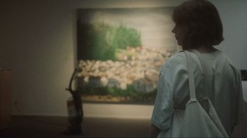 Movie still from “Showing Up” (2022), directed by Kelly Reichardt – A woman standing in front of a painting in an art gallery; Medium shot, Low angle
